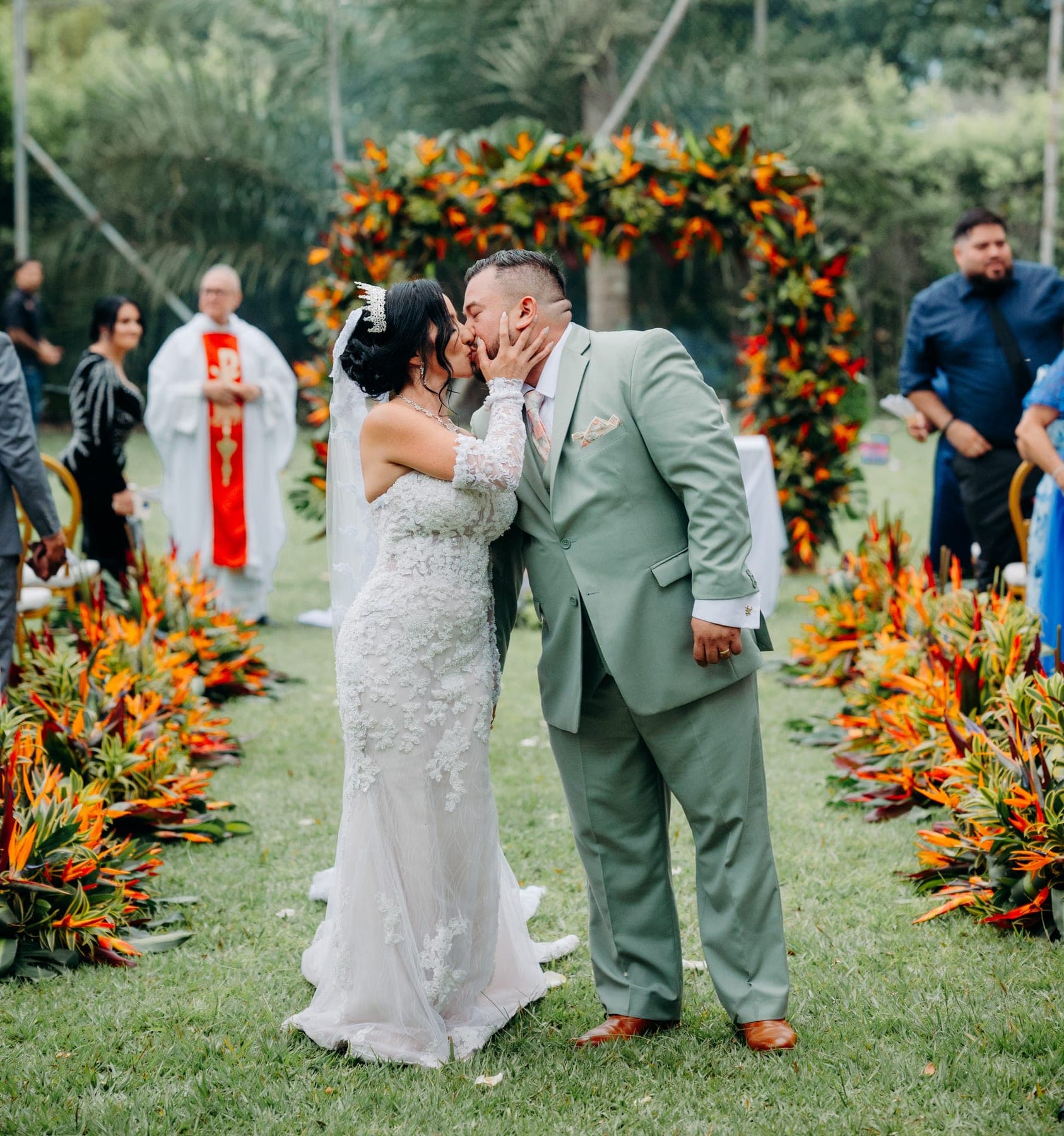 Cinthya y Will se besan al final de su ceremonia bajo un arco de flores tropicales