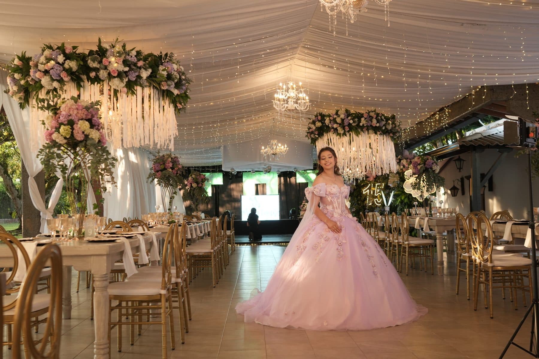 Quinceañera en un salón con lámparas de cristal y techo de luces
