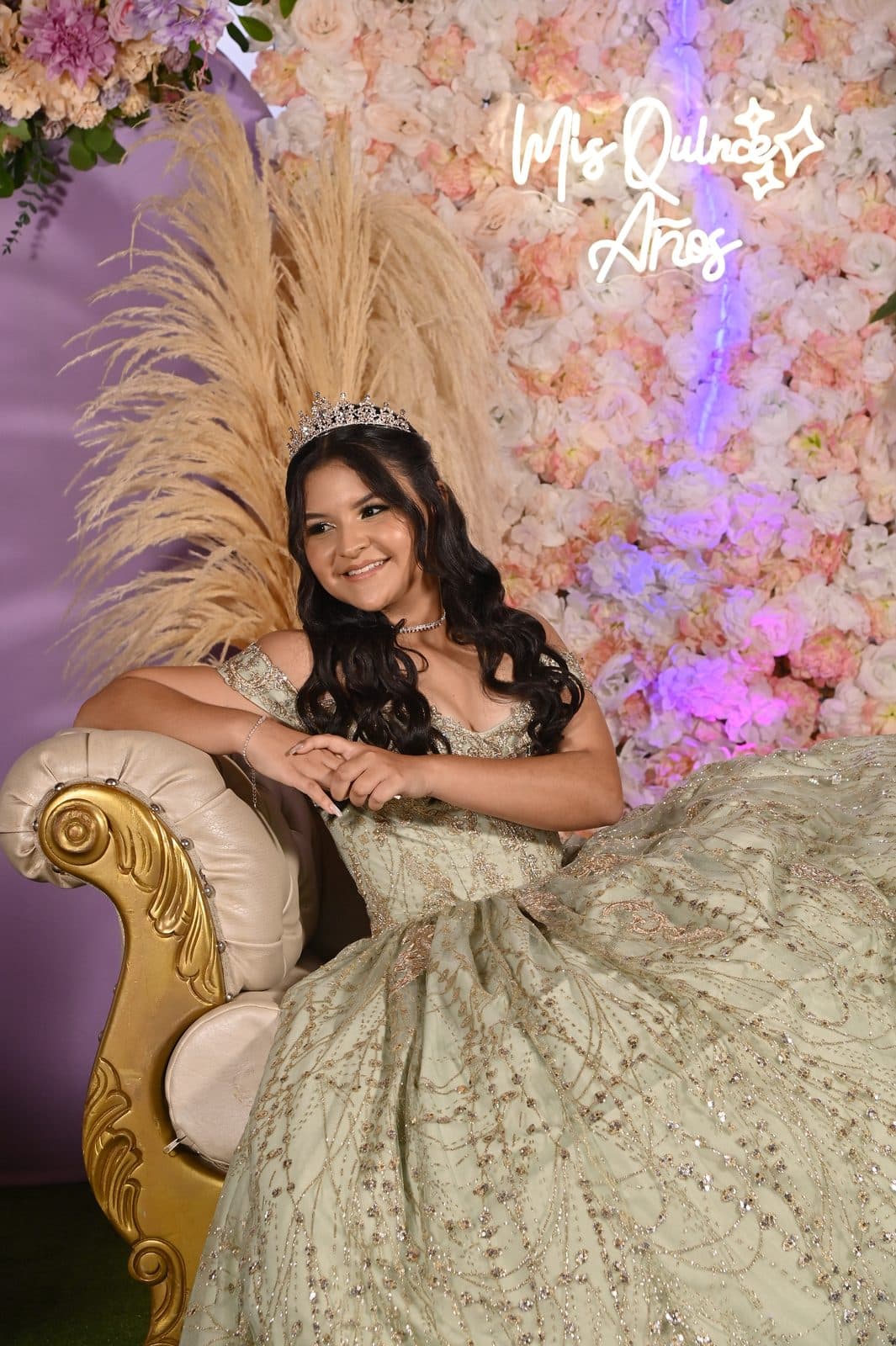 Quinceañera sentada en una poltrona dorada entre flores y pampas