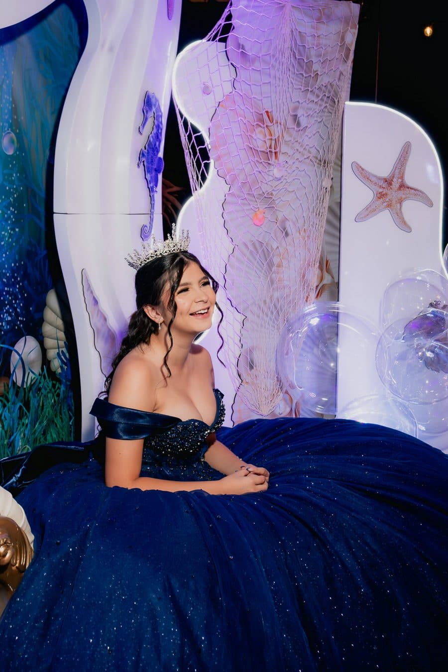 Quinceañera con vestido azul en un trono de conchas y perlas